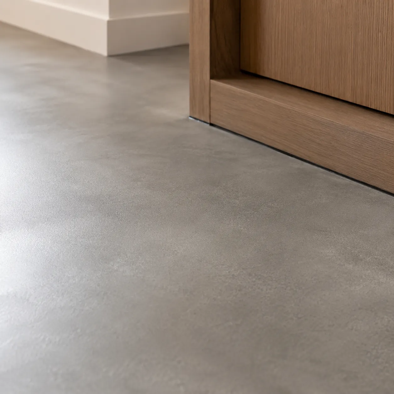 Close-up of a polished grey cement screed floor meeting a timber skirting, showing the smooth, seamless surface finish