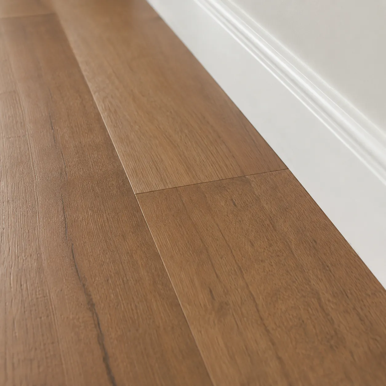 Close-up of wide-plank wood flooring with visible grain and plank seams, meeting a white skirting board